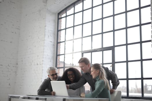 A group of professionals collaborating energetically around a laptop in a bright, airy office.