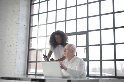 Professional aged male entrepreneur consulting young female African American colleague during office work with laptop and smartphone inside industrial building