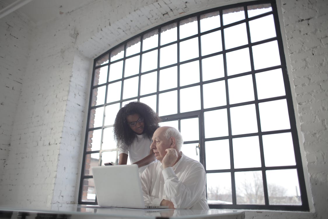 Free Professional aged male entrepreneur discussing startup project with young female African American colleague during office work with laptop and smartphone in workplace with industrial interior Stock Photo