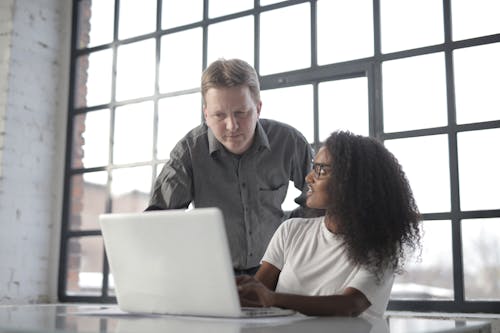 Free Professional adult male entrepreneur browsing netbook with young female African American colleague and discussing startup project during office work in workplace near big window Stock Photo