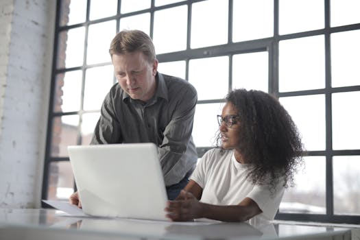 Two professionals collaborating on a laptop in a bright, modern office setting.