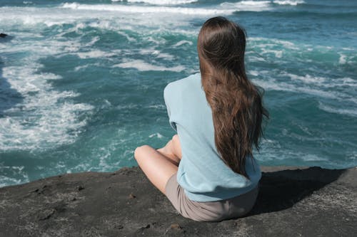 A Back View of a Woman Sitting on the Cliff Near the Ocean