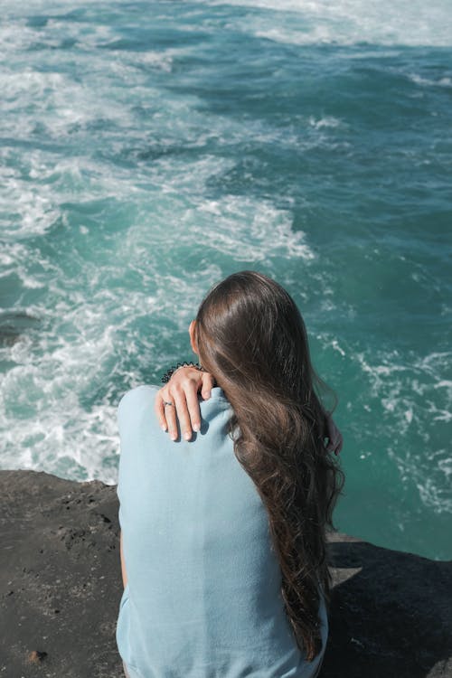 A Back View of a Woman Sitting Near the Ocean