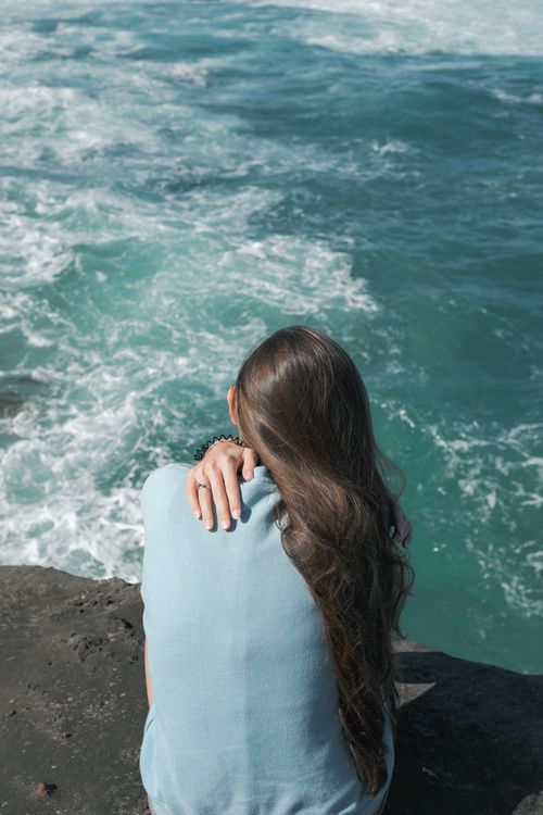 A Back View of a Woman Sitting Near the Ocean · Free Stock Photo