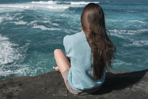 A Woman in Blue Shirt Sitting on the Cliff