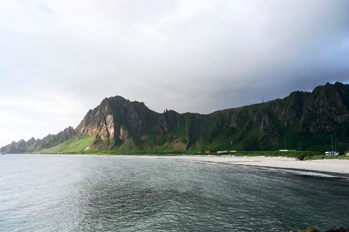 Free A stunning coastal landscape featuring a rugged mountain range and a serene beach under a cloudy sky. Stock Photo