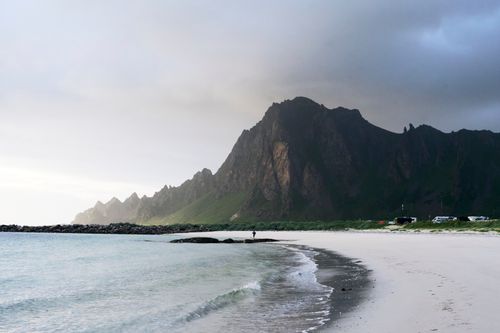 Free Explore a stunning landscape featuring a serene beach and towering mountains under dramatic skies. Stock Photo