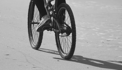Free Monochrome image of a cyclist riding a bicycle on a sandy beach, highlighting motion and texture. Stock Photo