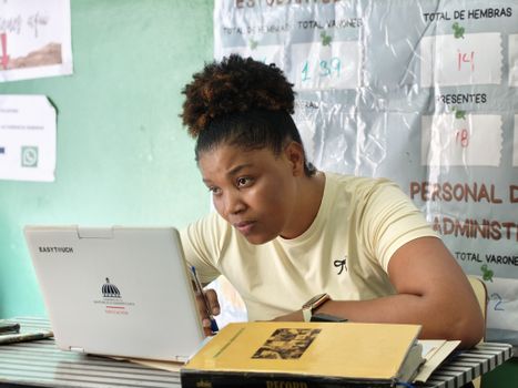 Woman concentrating on her laptop in an educational environment, surrounded by charts and notebooks.