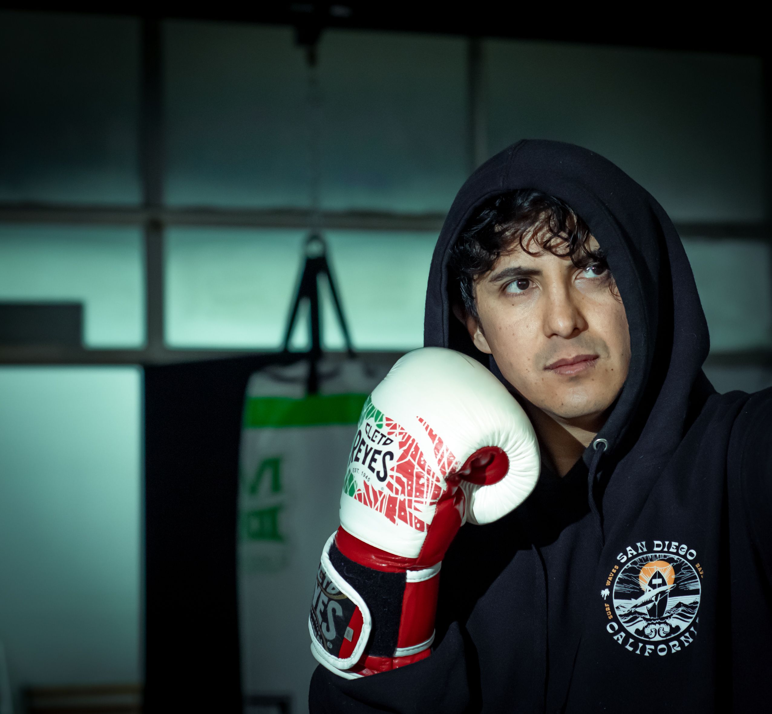 Focused young boxer wearing a hoodie and gloves during training session indoors.