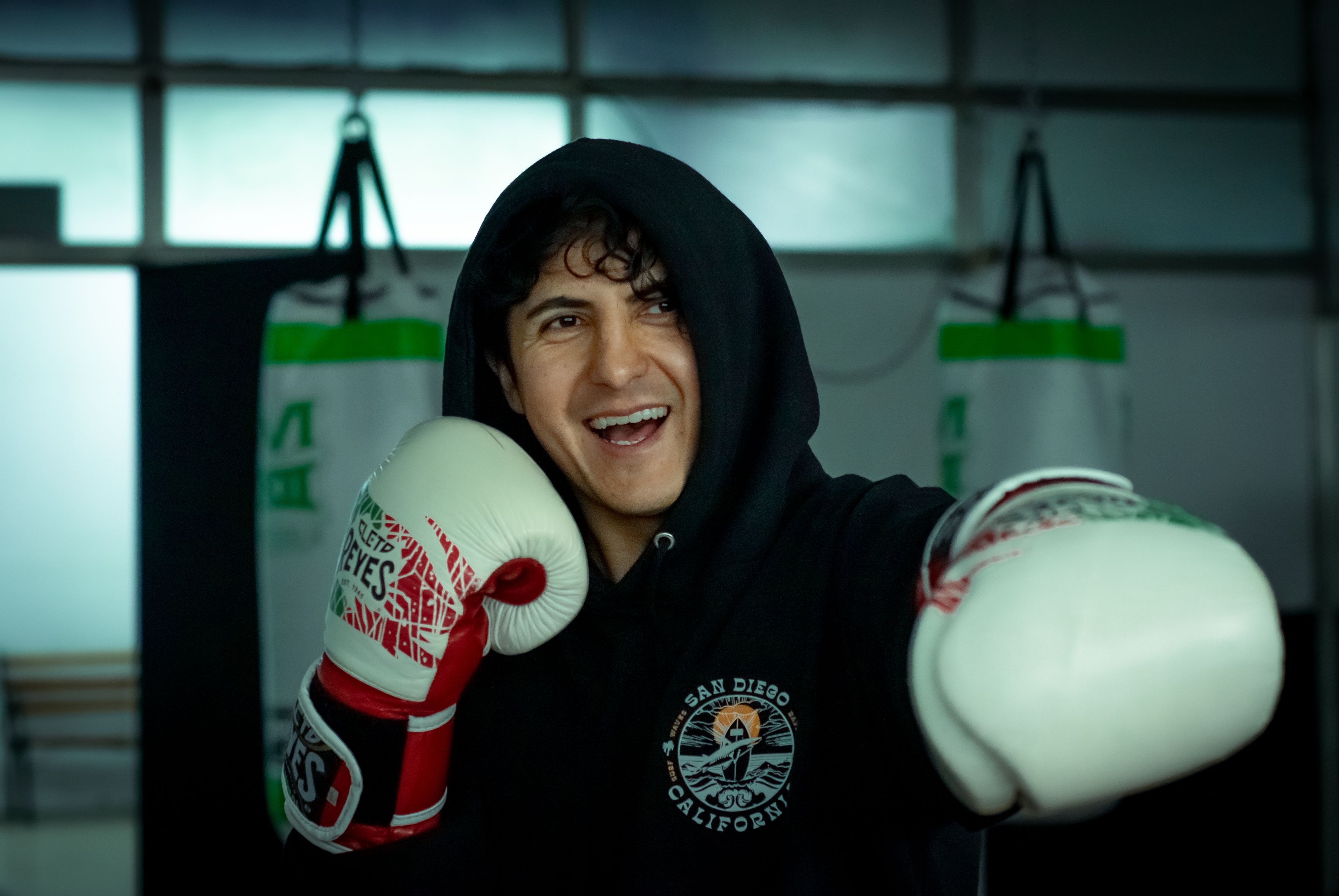 Smiling young boxer posing confidently with gloves in an indoor gym setting.
