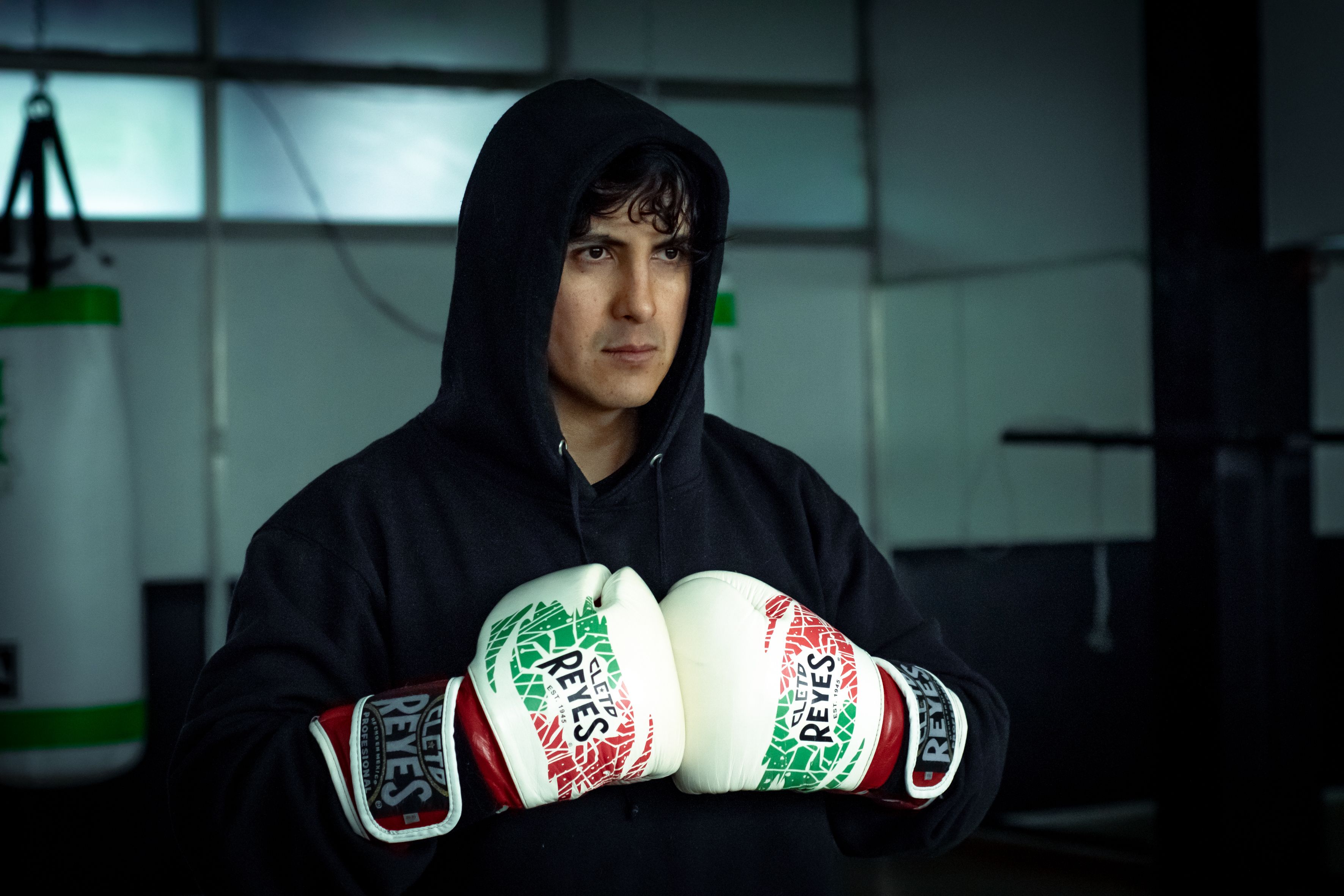 A boxer wearing a hoodie and gloves stands ready for training indoors.