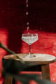 A crisp splash of water into an elegant crystal glass against a vivid red backdrop.