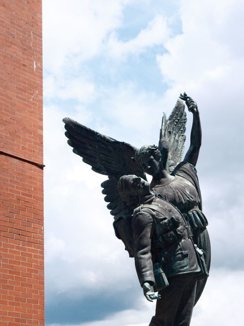 Free Statue of an angel aiding a fallen soldier under a cloudy sky. Stock Photo