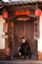 Man in Black Jacket and Black Sunglasses Sitting Outside Brown Wooden Door