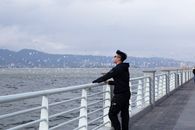 一个男人穿着休闲服，站在码头栏杆上，凝视着大海和远山