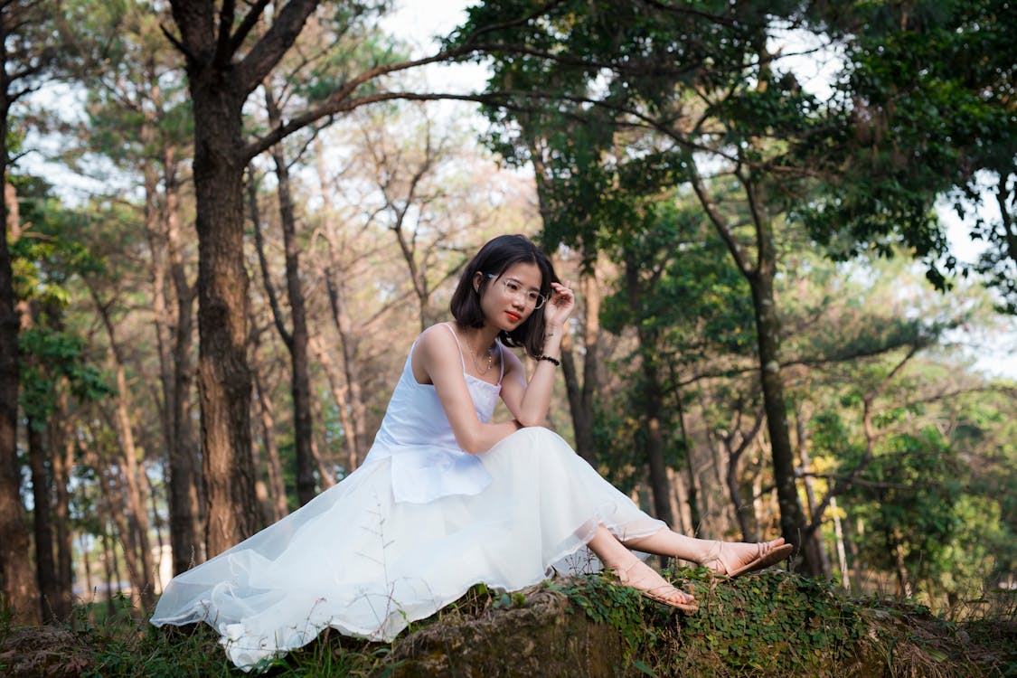 Free Woman in White Dress Wearing Eyeglasses Sitting Under Tree Stock Photo