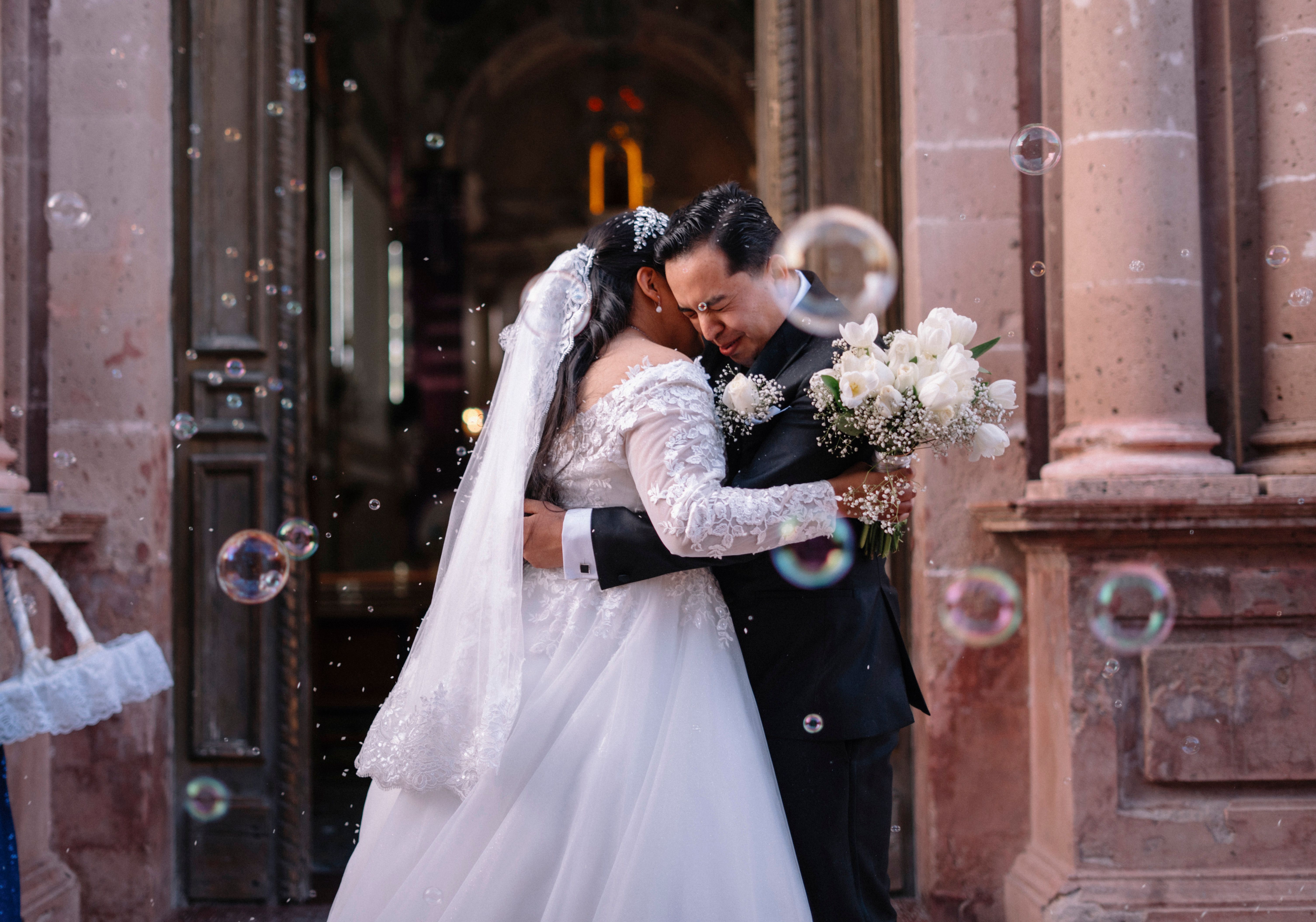 A newlywed couple shares a heartfelt embrace surrounded by bubbles at a historic venue.