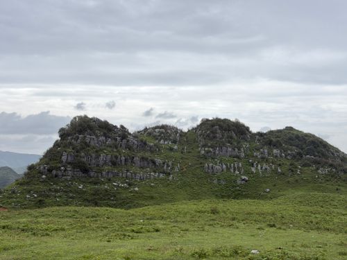 Free Lush green hill landscape with rocky formations under an overcast sky, serene natural scenery. Stock Photo