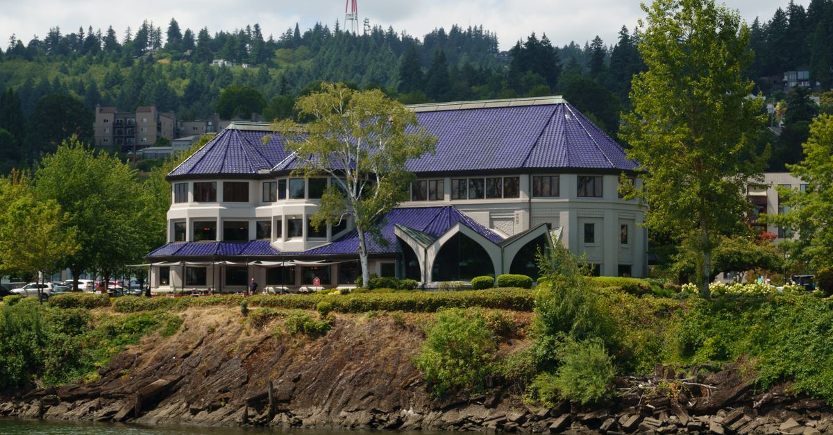 A modern building with a striking blue roof by a river surrounded by lush greenery.
