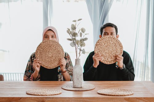 A Man and Woman Holding a Woven Placemats while Covering Face