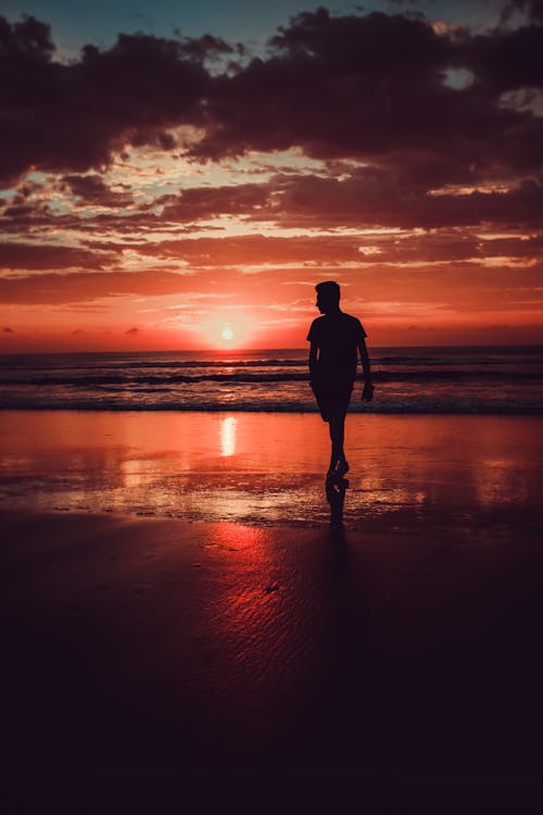 Schattenbild Des Mannes, Der Am Strand Während Des Sonnenuntergangs Steht