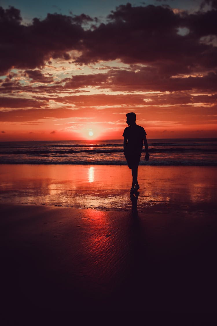 Silhouette Of Man Standing On Beach During Sunset