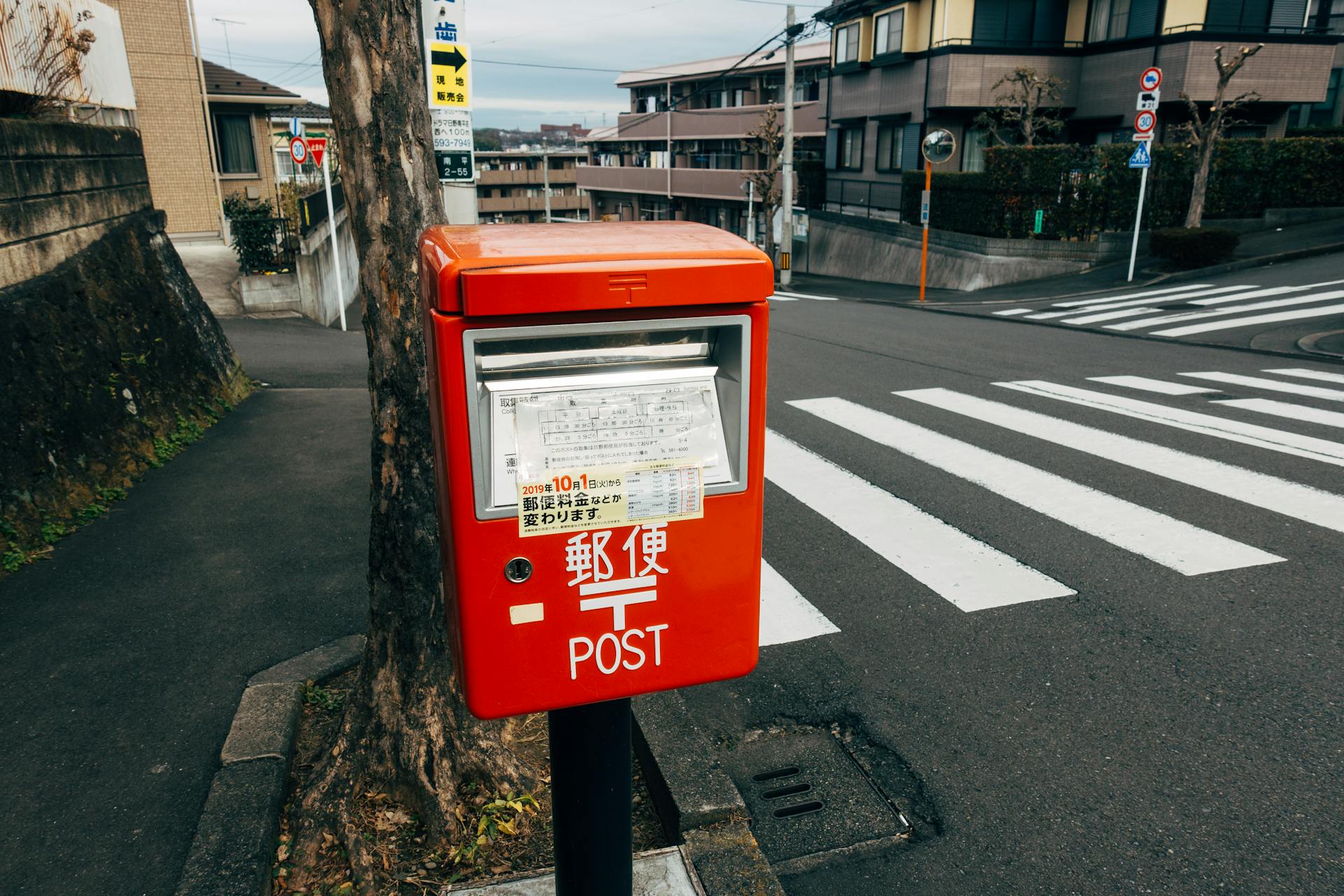Bright red mailbox by crosswalk in Japanese urban neighborhood.