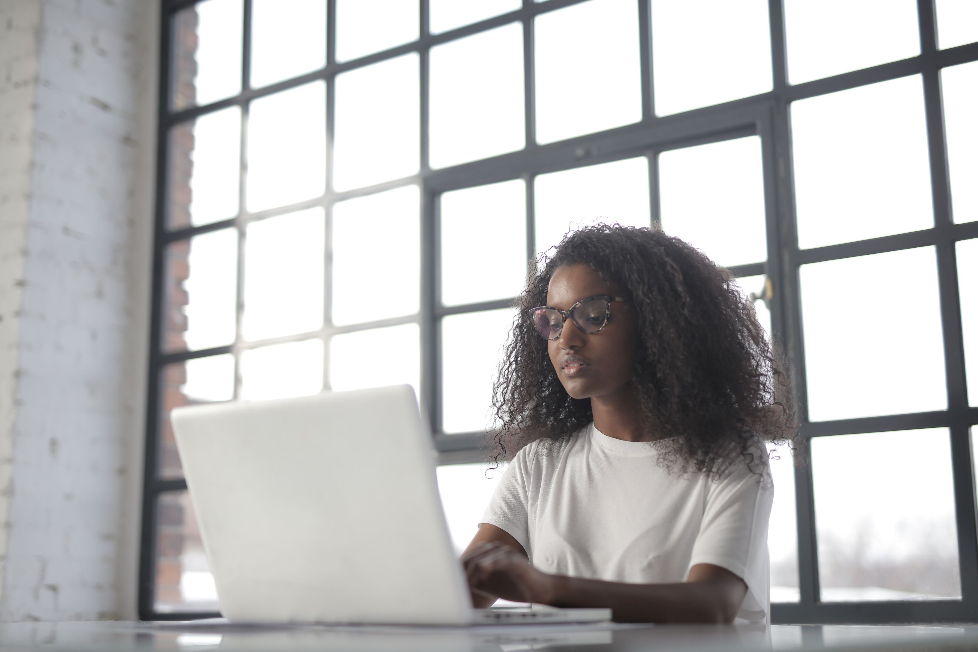 Focused young woman wearing glasses working on a laptop at a bright and modern workspace.