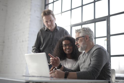 Positive multiethnic coworkers of different ages in casual clothes sitting at table and browsing netbook while working on project together