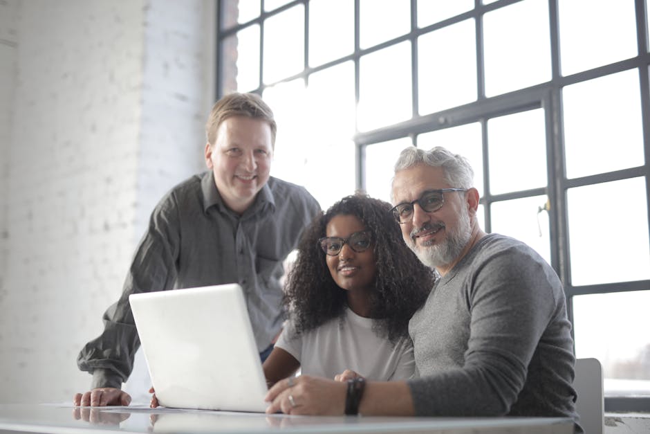 Optimistic diverse managers in casual wear smiling at camera while using computer and discussing details of work in light office