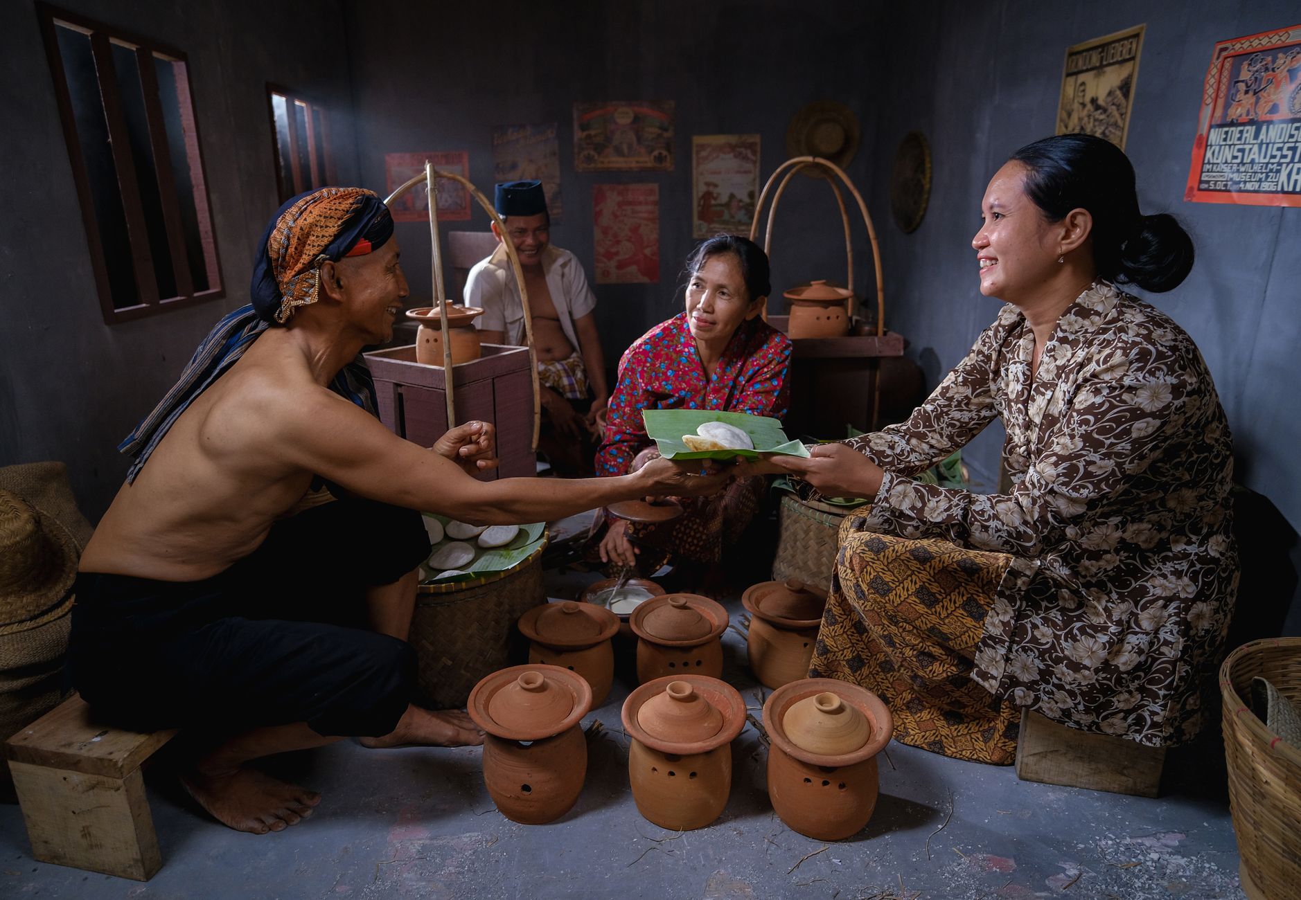Four people in traditional attire inside a Javanese kitchen preparing food.