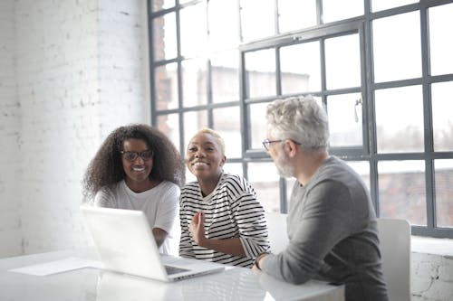 Positive multiracial colleagues wearing informal clothes and working on project together while surfing Internet on computer in modern office