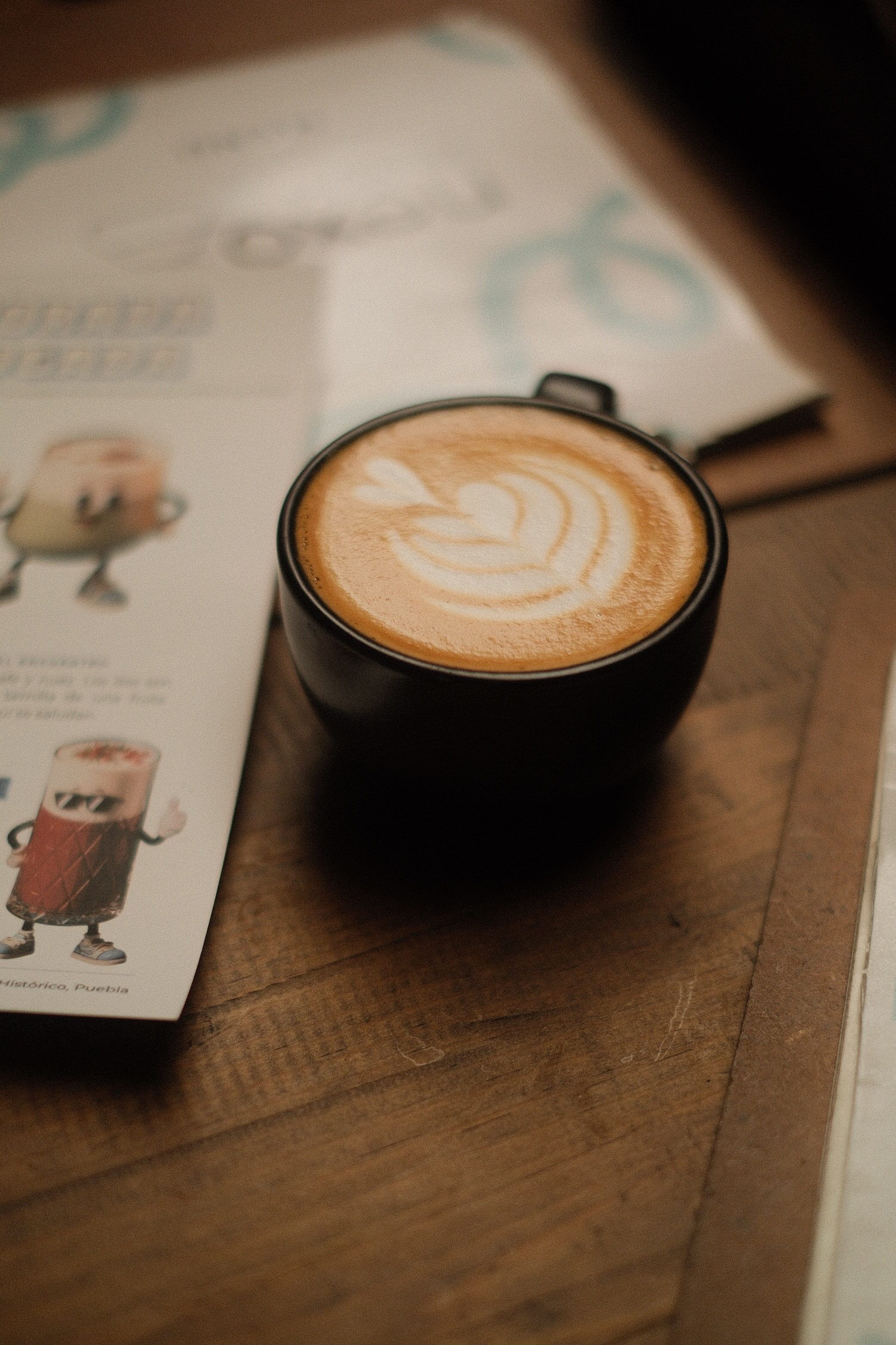 A beautifully crafted latte with art foam design sits on a warm wooden table in a cozy cafe.