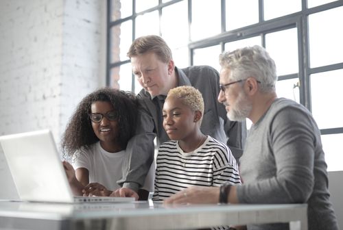 Free Group of smiling diverse group of people wearing informal clothing and watching video on netbook while spending time together in afternoon Stock Photo