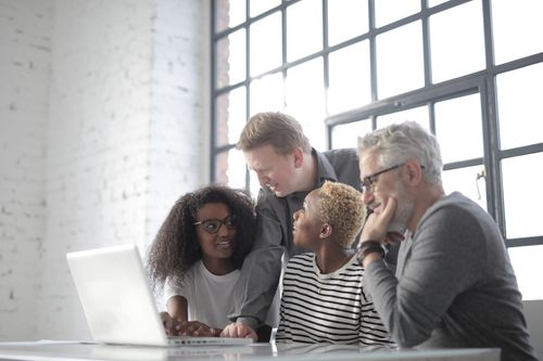 Free Concentrated multiracial coworkers of different ages in casual wear sitting at table and discussing details of project while working on computer in light office Stock Photo