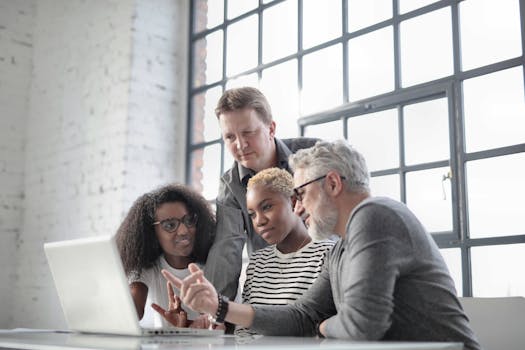 Multiracial colleagues of different ages sitting at table in modern workplace while watching project on laptop and discussing with active gesticulation