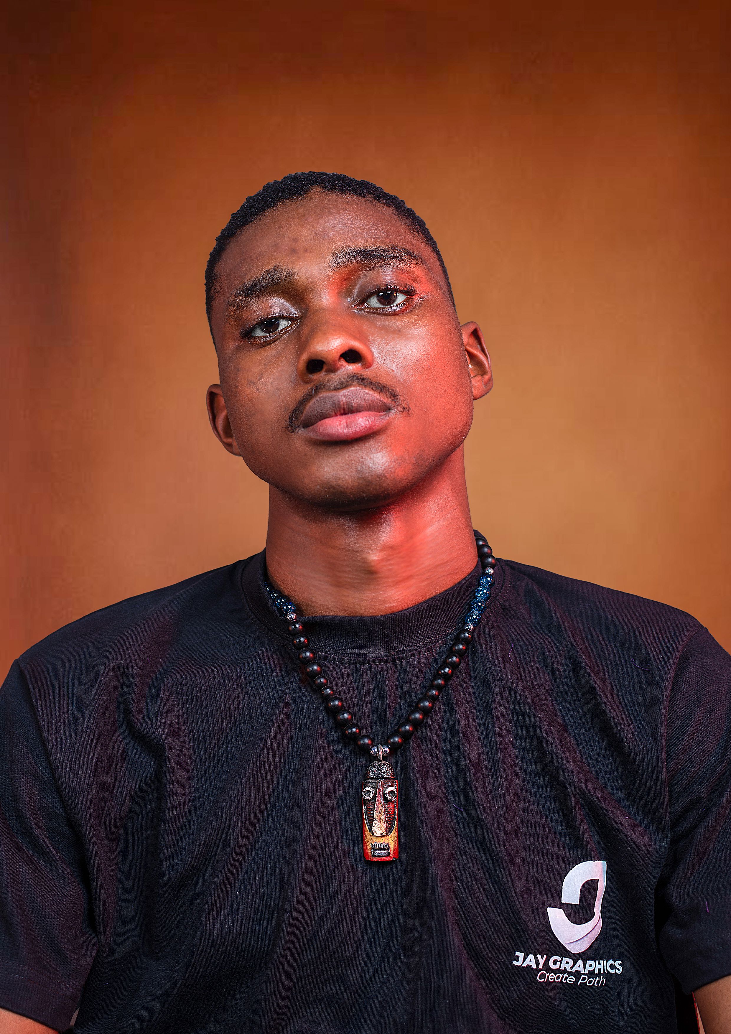 A thoughtful portrait of a man against a warm backdrop wearing a beaded necklace.