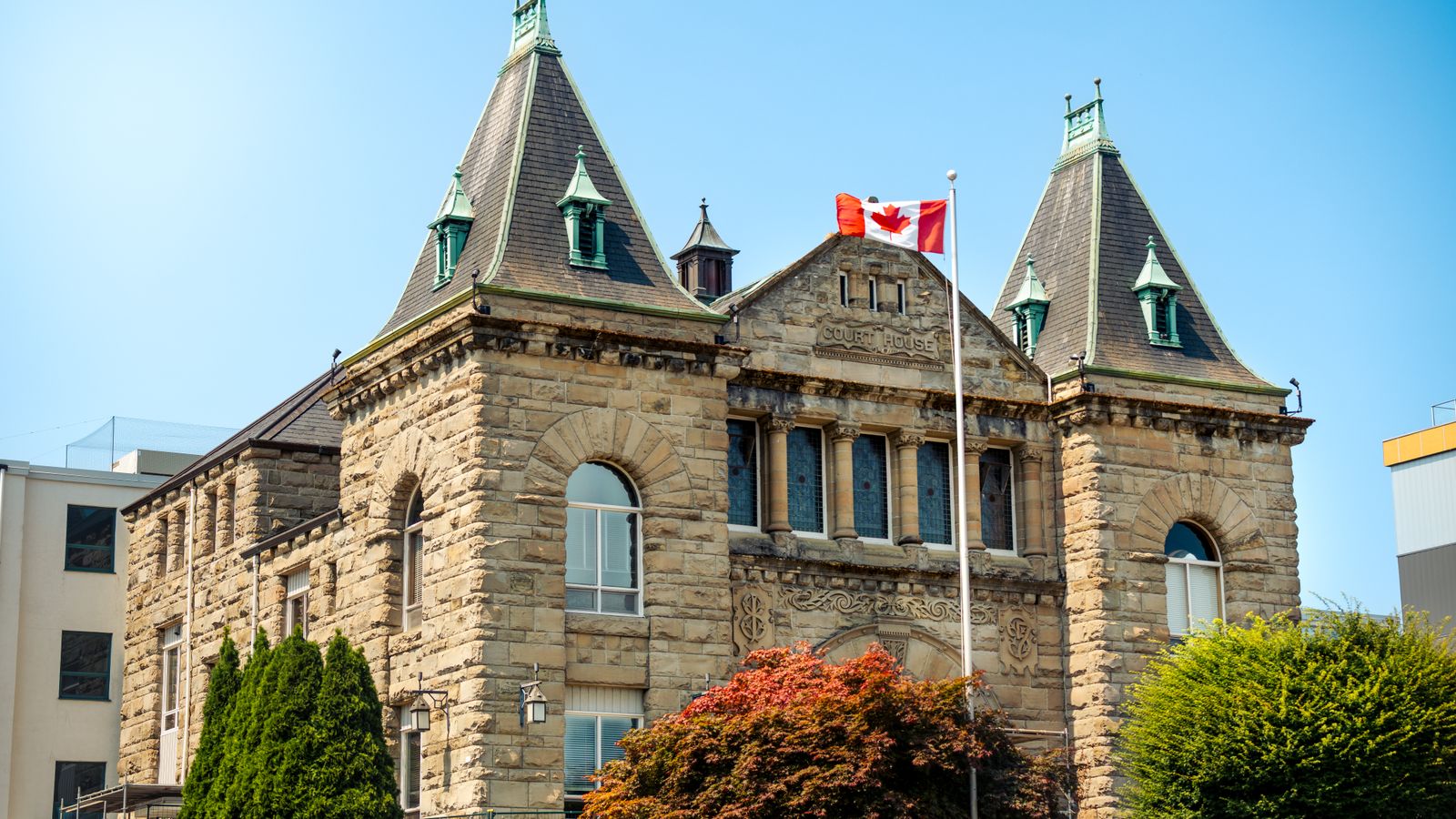 A classic stone courthouse in Nanaimo, British Columbia, with Canadian flag, under clear blue sky.