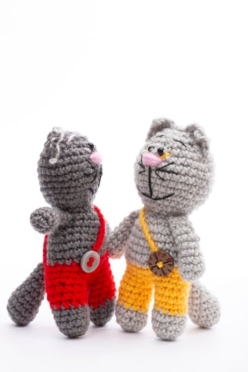 Free Two crocheted cat dolls dressed in vibrant red and yellow overalls, posing together. Stock Photo