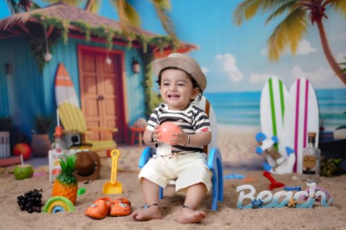 Free Adorable toddler sitting on a sandy beach setting with toys and a colorful backdrop. Stock Photo