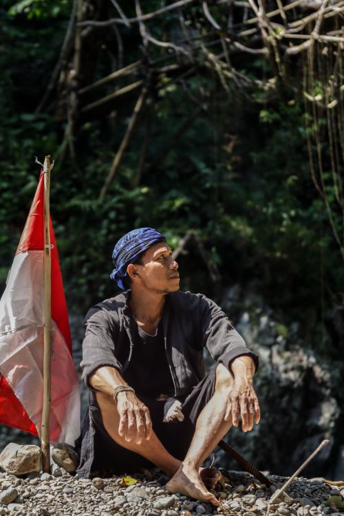 Free Man sitting next to Indonesian flag outdoors, looking contemplative in nature Stock Photo