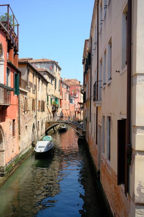 Free Explore a scenic Venetian canal with vibrant buildings and a small boat under clear skies. Stock Photo