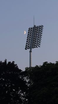 Stadium floodlights silhouetted against evening sky and crescent moon.