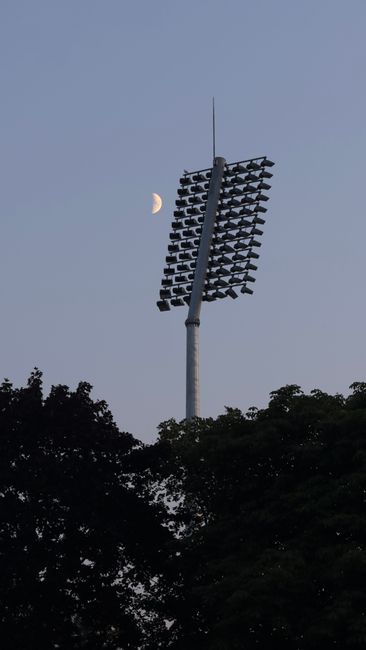 Stadium floodlights silhouetted against evening sky and crescent moon.