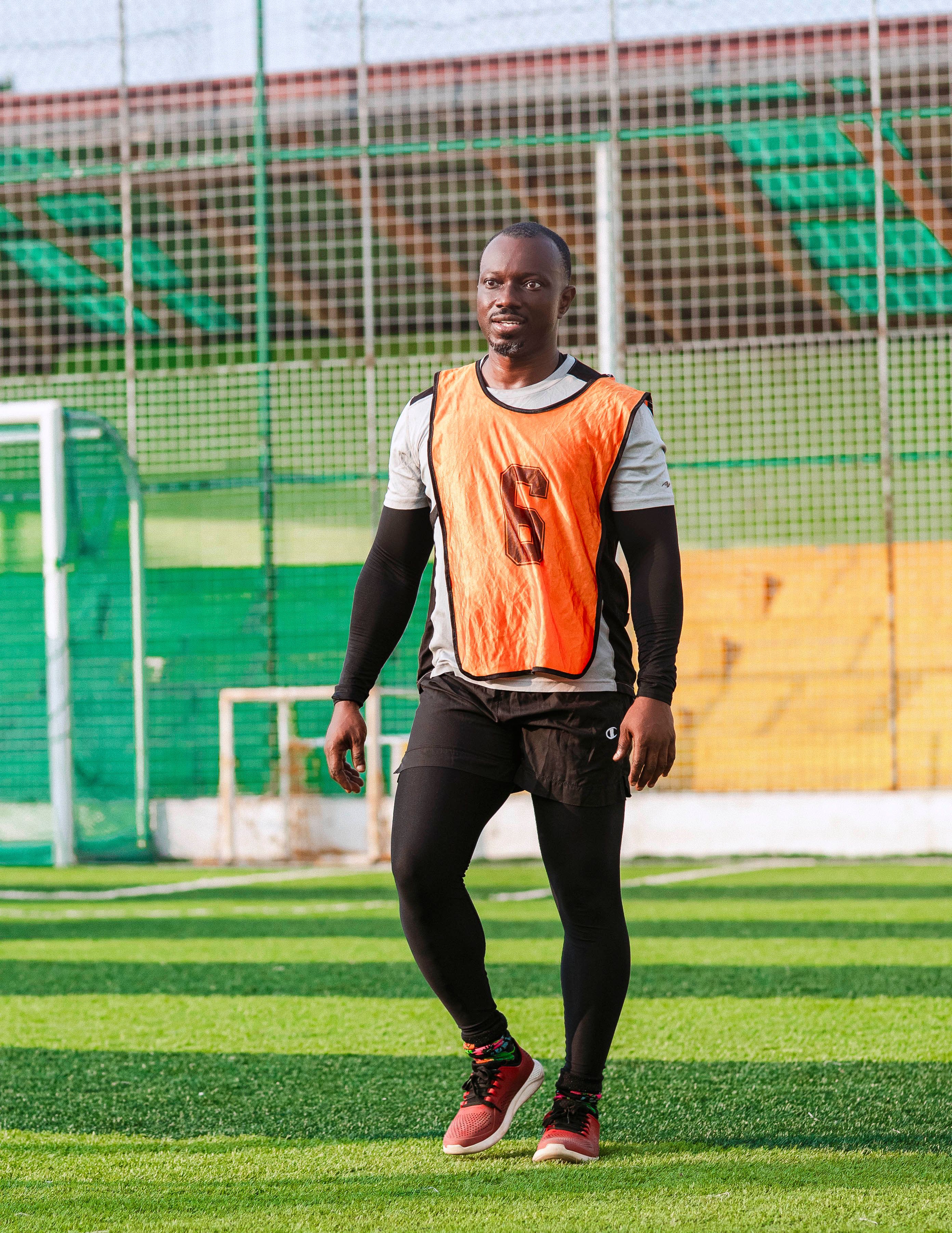Athlete in orange vest walking on sunny sports field
