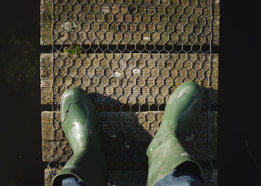 Overhead view of green rubber boots on a weathered wooden bridge.