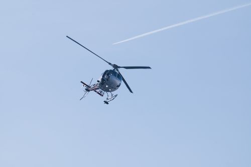 Free A helicopter flying in a clear blue sky with a visible contrail. Stock Photo