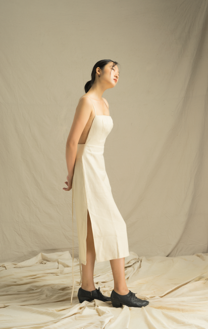 A woman in a sleek white dress and black shoes poses elegantly in a studio setting.