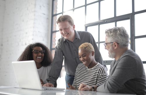 Free Group of diverse people laughing and using netbook while working on project together in office with white brick walls and big window Stock Photo